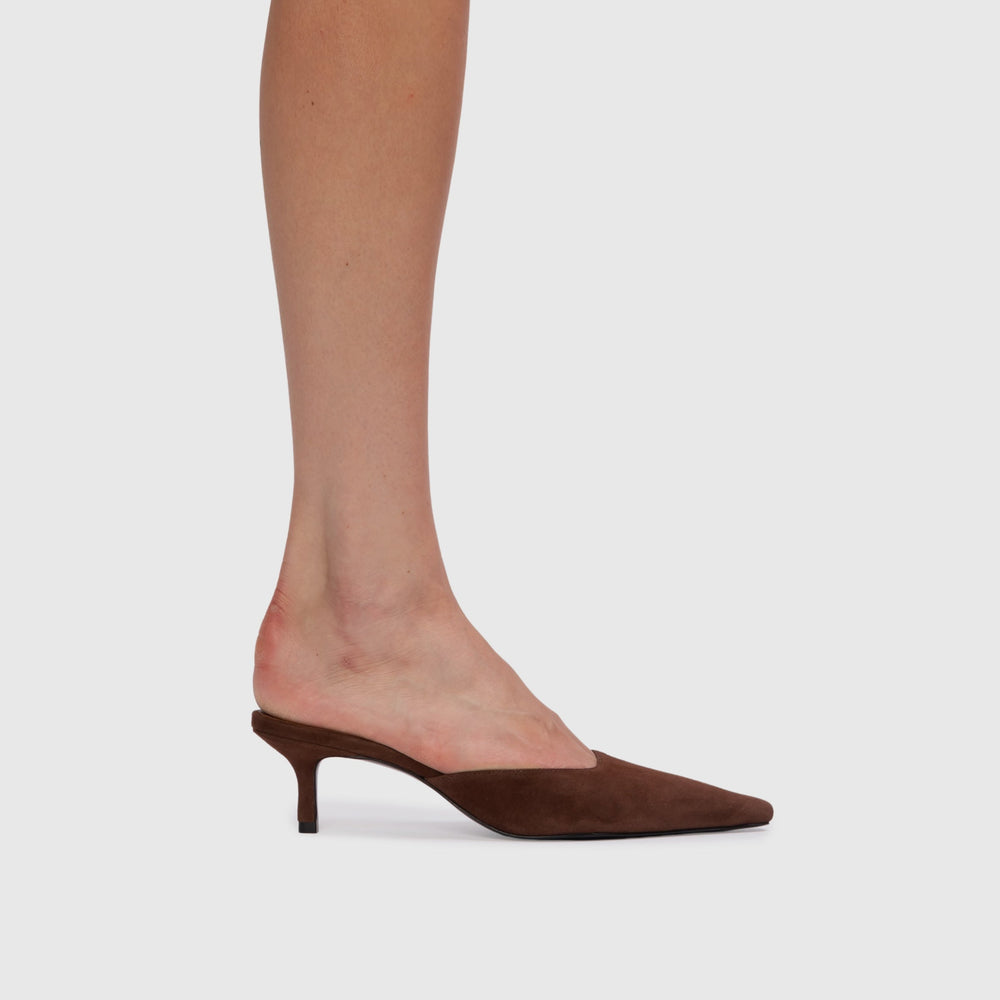 Brown suede high-heeled shoe worn by a person on a light gray background