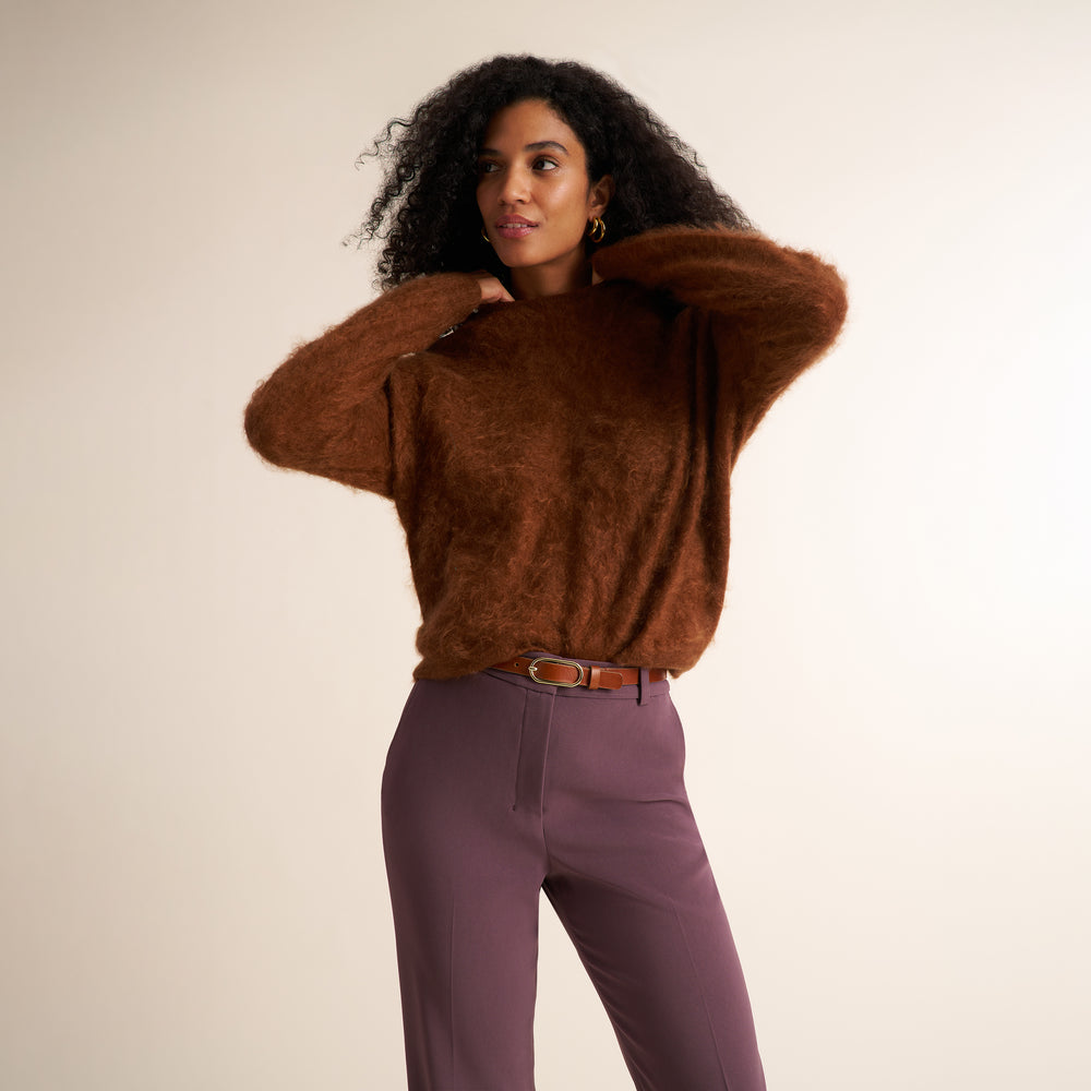Woman wearing a rust colored sweater with hazy mauve purple pants and cognac and gold belt