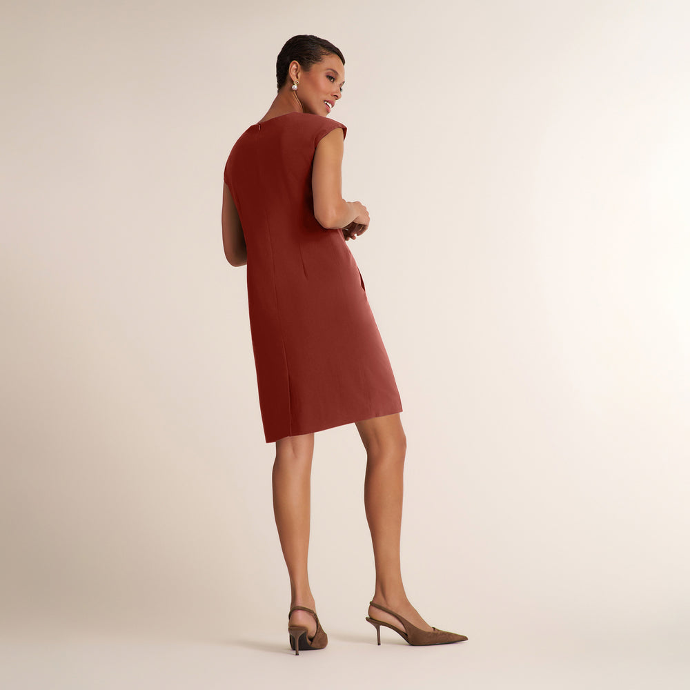 A woman modeling a sleeveless, knee-length rust-colored dress from the back, paired with brown slingback heels, against a solid light beige studio background.