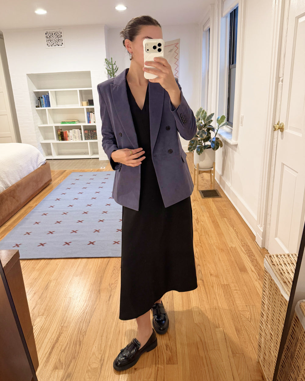 Person taking a mirror selfie wearing a purple blazer and black skirt in a room with wooden flooring.
