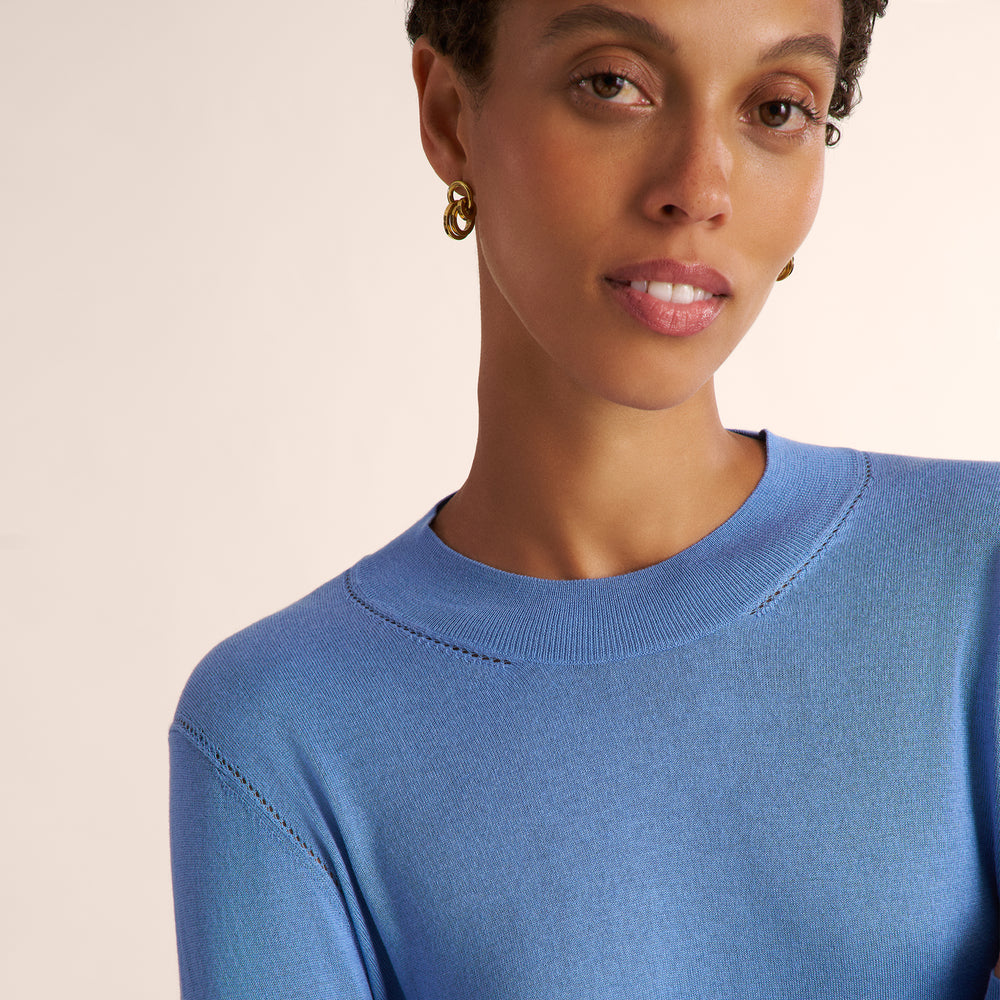 Woman wearing a blue splendor color long sleeve sweater with black wide leg pants and matching blazer