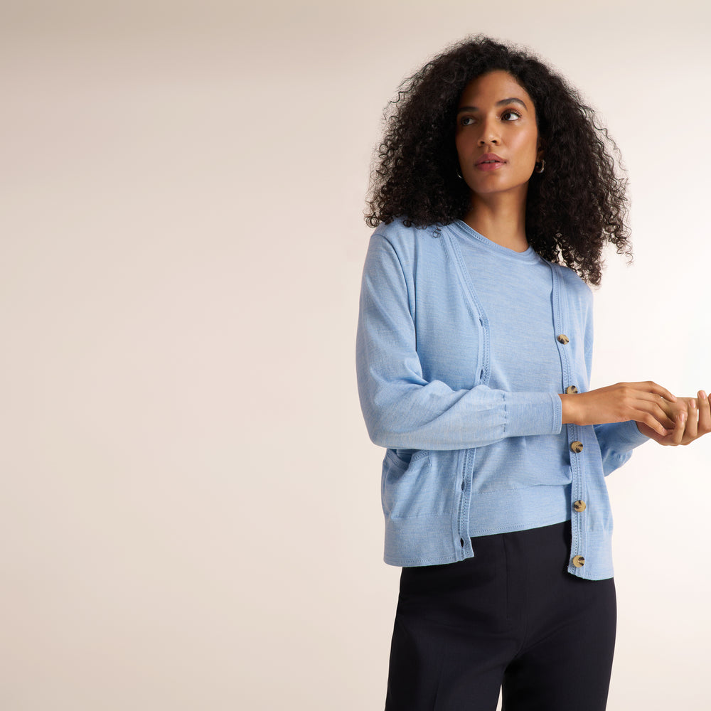 Woman wearing alight blue short sleeve sweater tank with a matching cardigan and wide leg white jeans