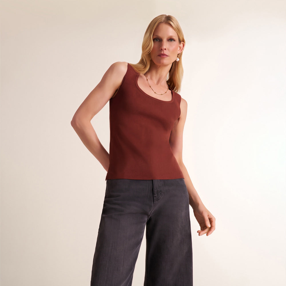 A woman modeling a sleeveless scoop-neck knit top in a muted reddish-brown color, paired with dark gray wide-leg jeans, against a plain light beige studio background.