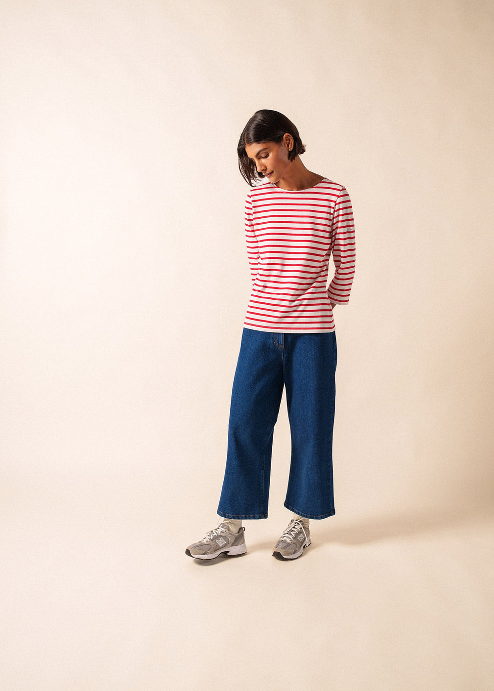 Woman wearing a red and white striped shirt and blue jeans on a beige background
