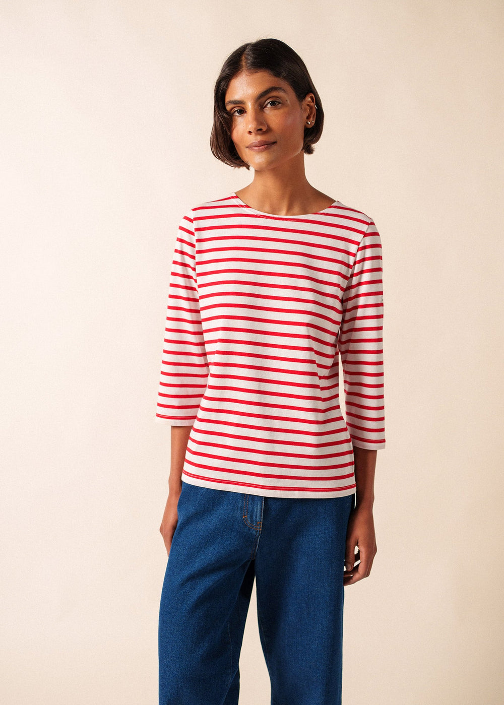 Woman wearing a red and white striped shirt with blue jeans on a beige background