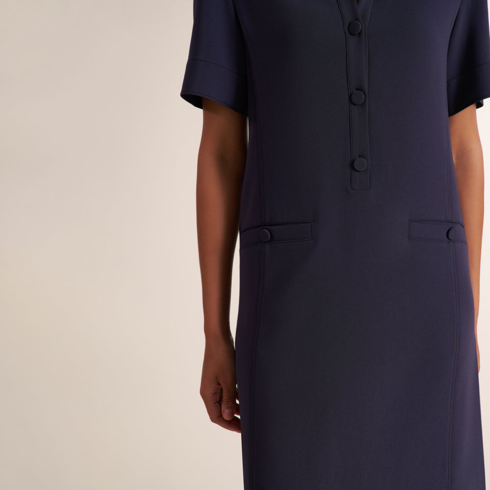 Woman wearing a collared short sleeve shift dress with covered buttons and pockets