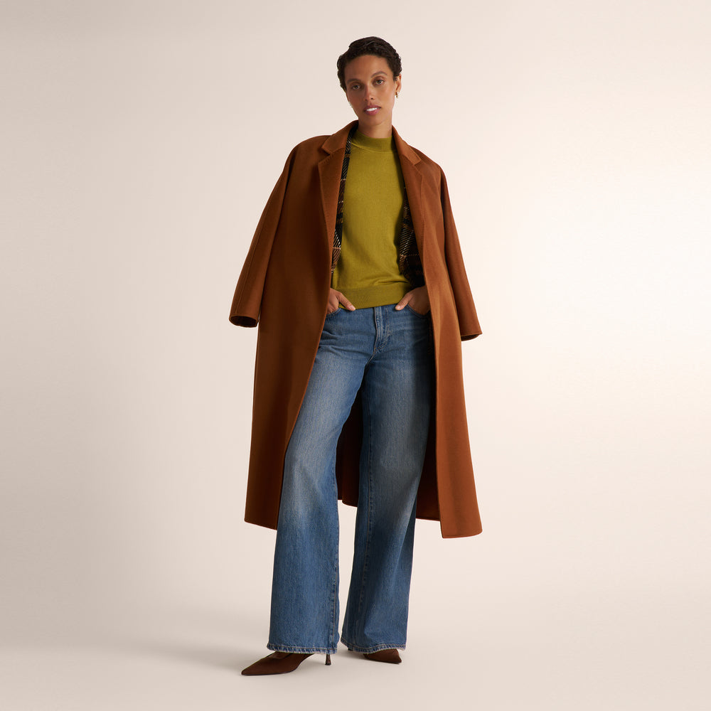 Woman wearing an olive green color short sleeve sweater with wide leg jeans and a plaid brown blazer and orange brown suede coat