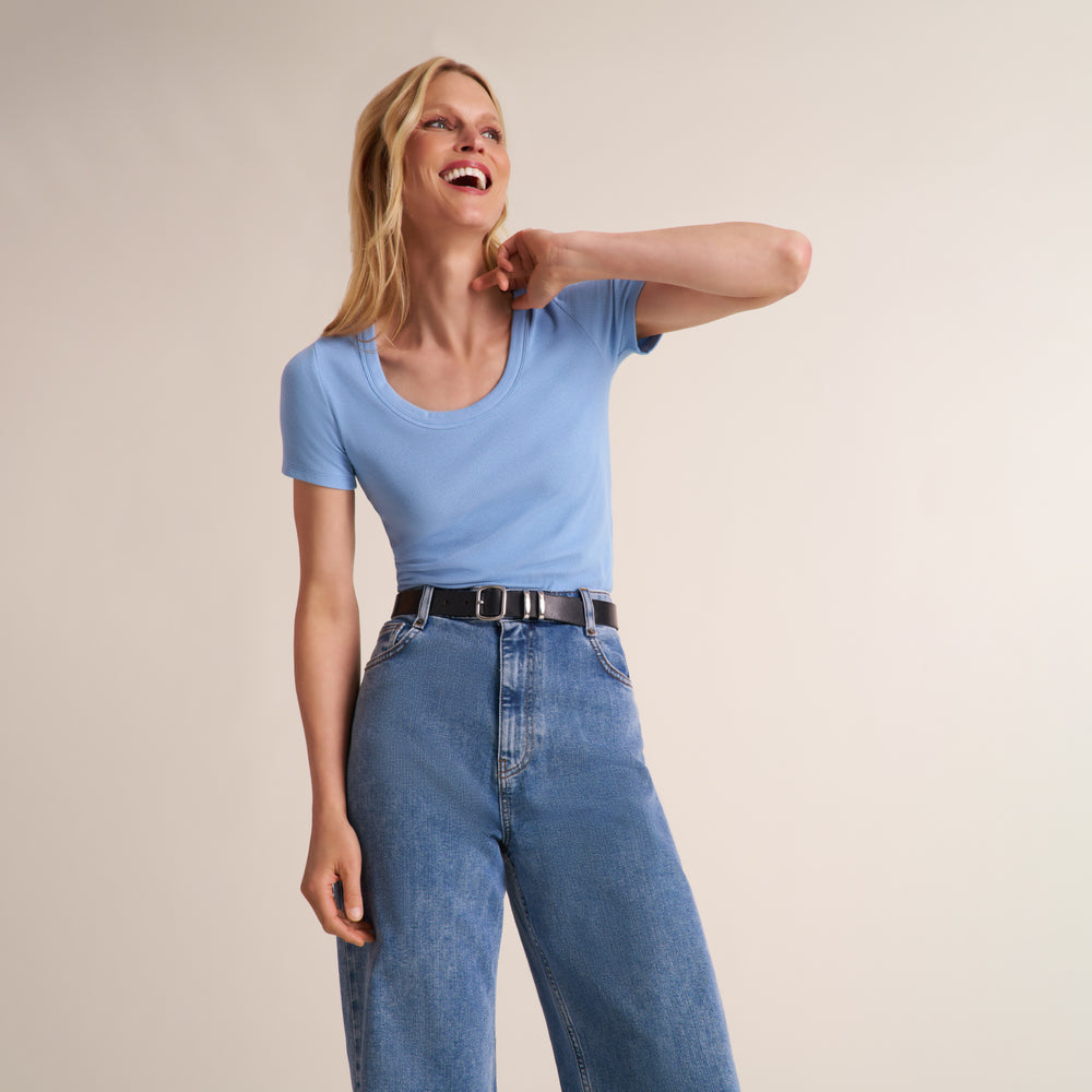 Woman wearing a light blue scoop neck short sleeve t-shirt with jeans and a belt