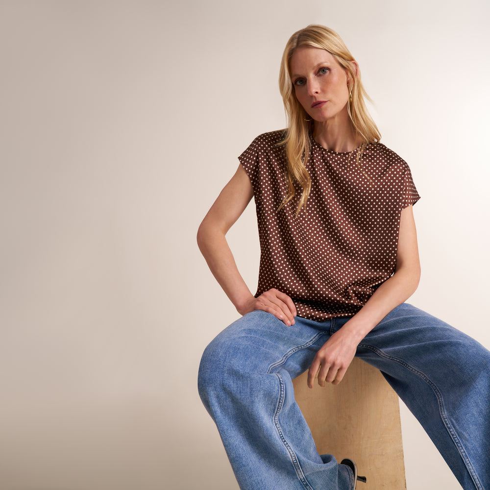 Woman wearing a pair of jeans with a cap sleeve top in a brown and white dot print