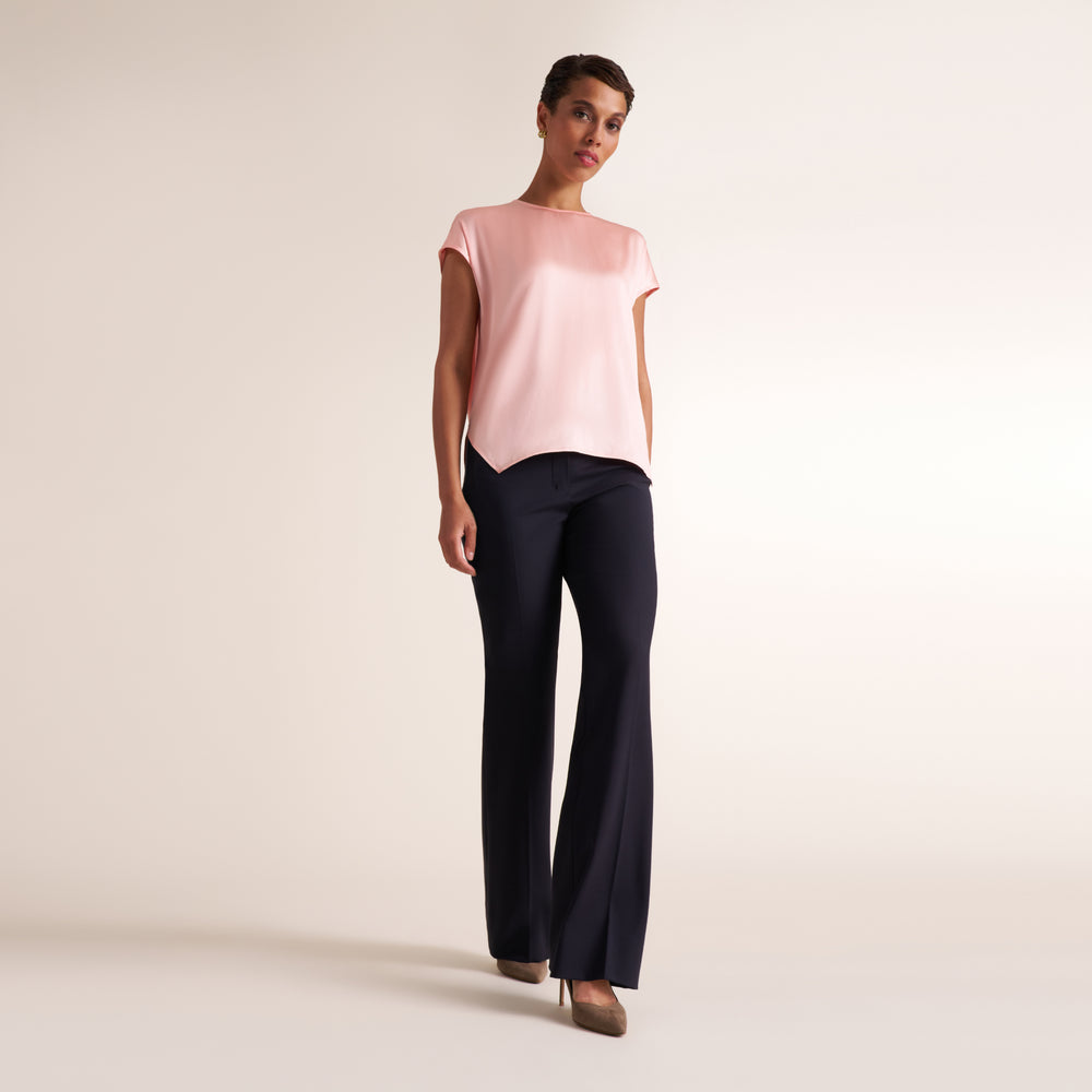 Woman wearing a flowy crew neck cap sleeve light pink silk charmeuse top with wide leg navy pants