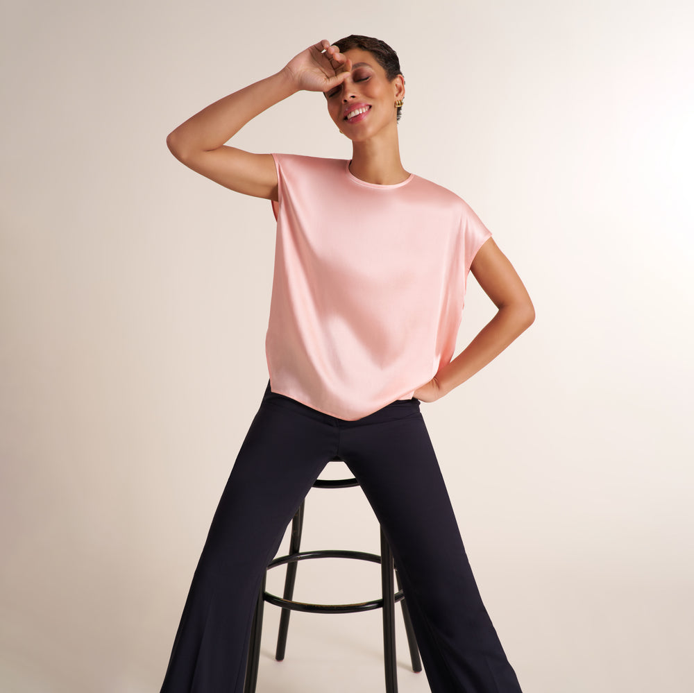Woman wearing a flowy crew neck cap sleeve light pink silk charmeuse top with wide leg navy pants