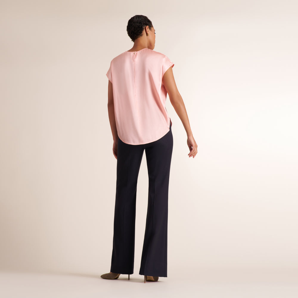 Woman wearing a flowy crew neck cap sleeve light pink silk charmeuse top with wide leg navy pants