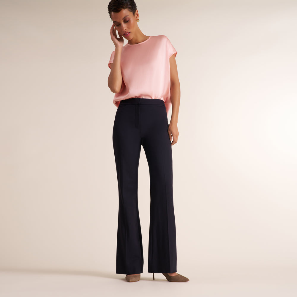 Woman wearing a flowy crew neck cap sleeve light pink silk charmeuse top with wide leg navy pants