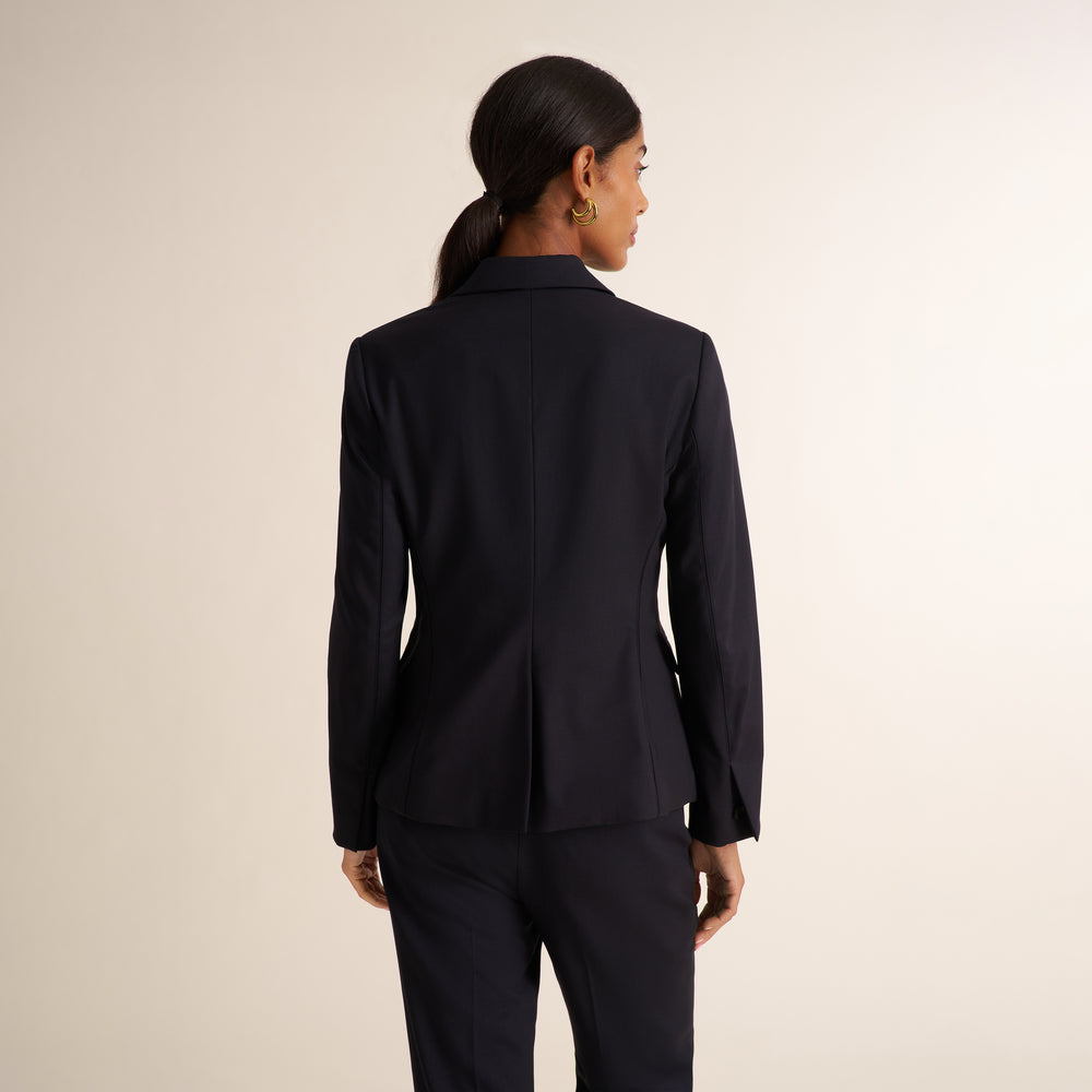 Woman wearing a black blazer, wide leg black suit pants, and a v-neck white tank top standing on a beige background