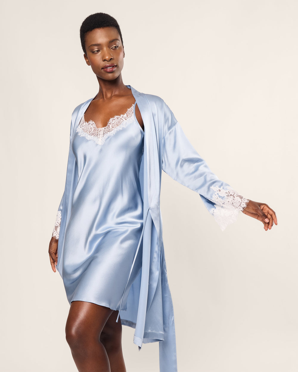 Woman wearing a light blue satin robe with lace trim on a plain background