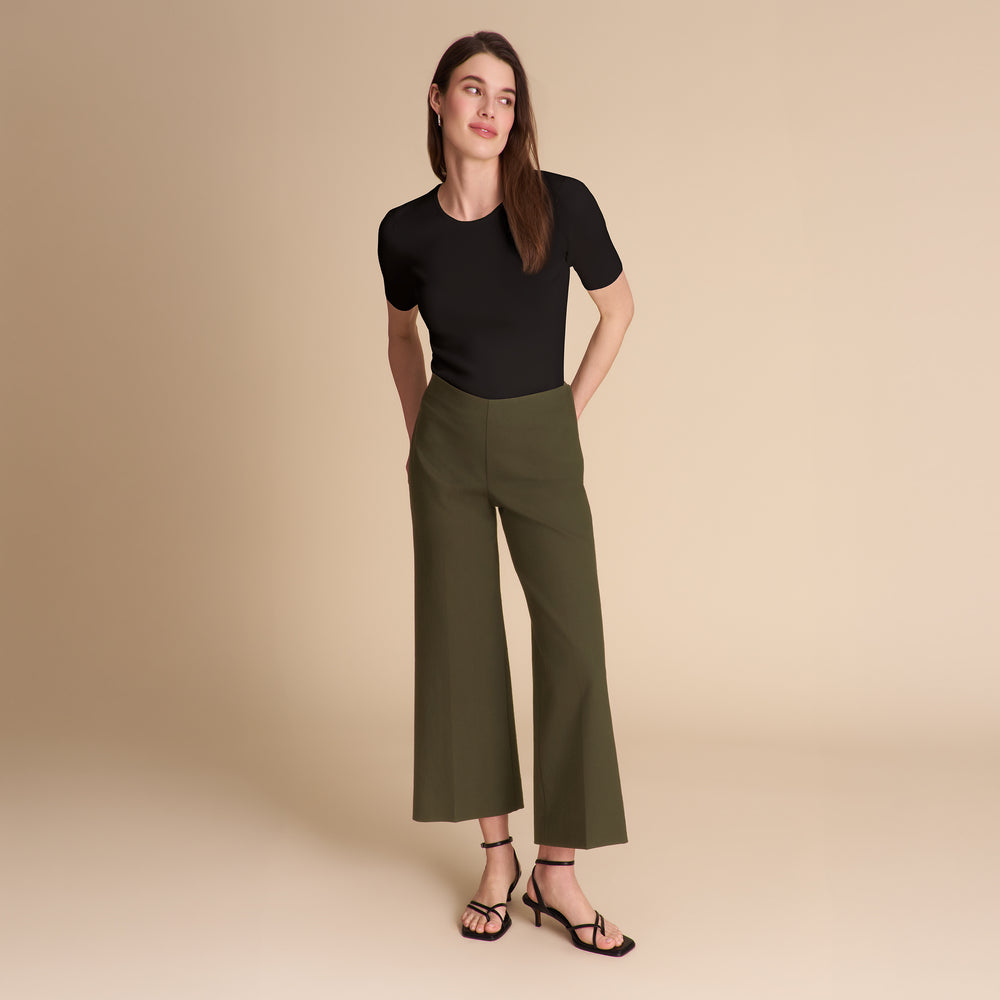 Woman wearing dark green pants and a black shirt on a beige background