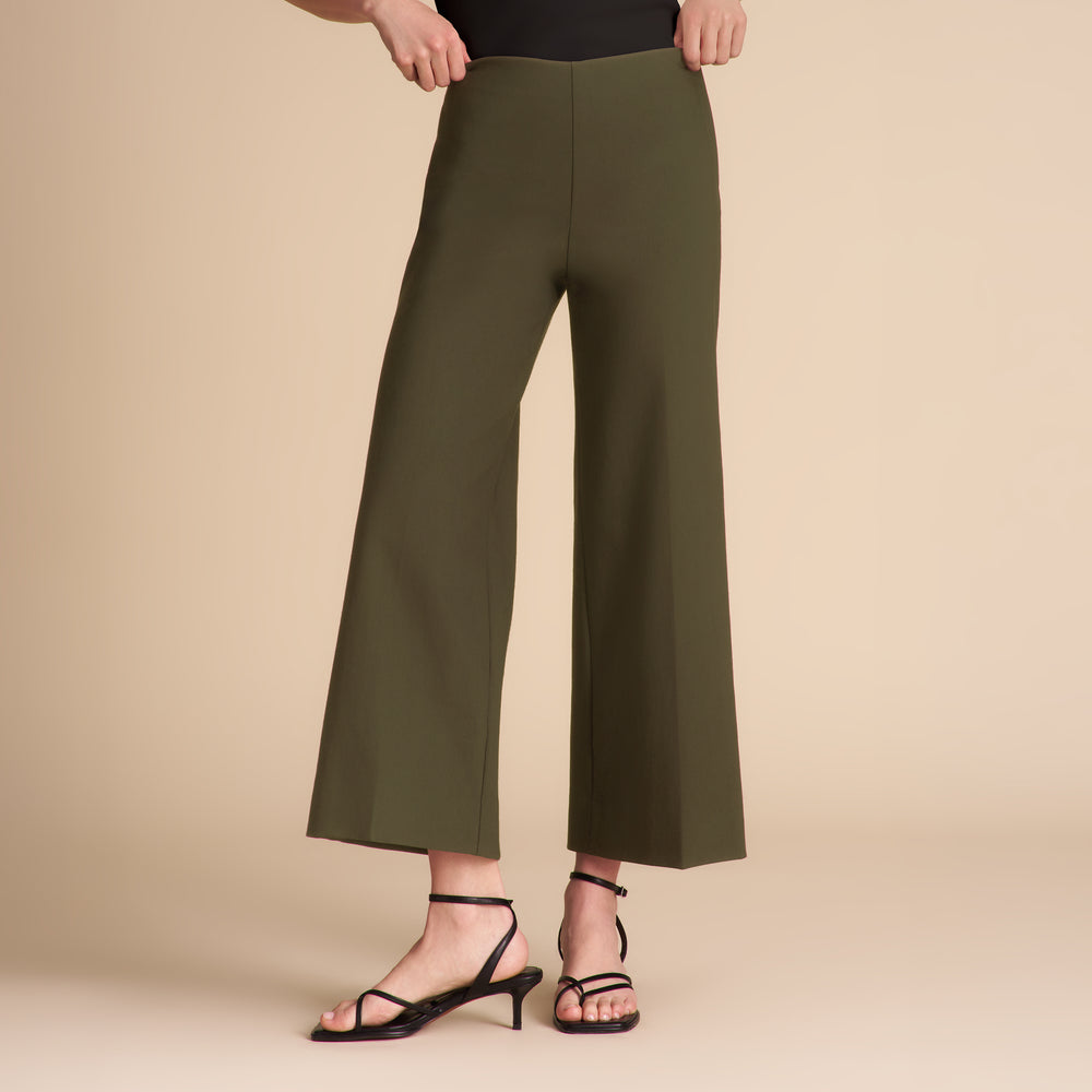 Woman wearing dark green pants and a black shirt on a beige background