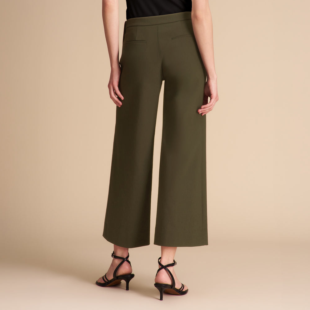 Woman wearing dark green pants and a black shirt on a beige background