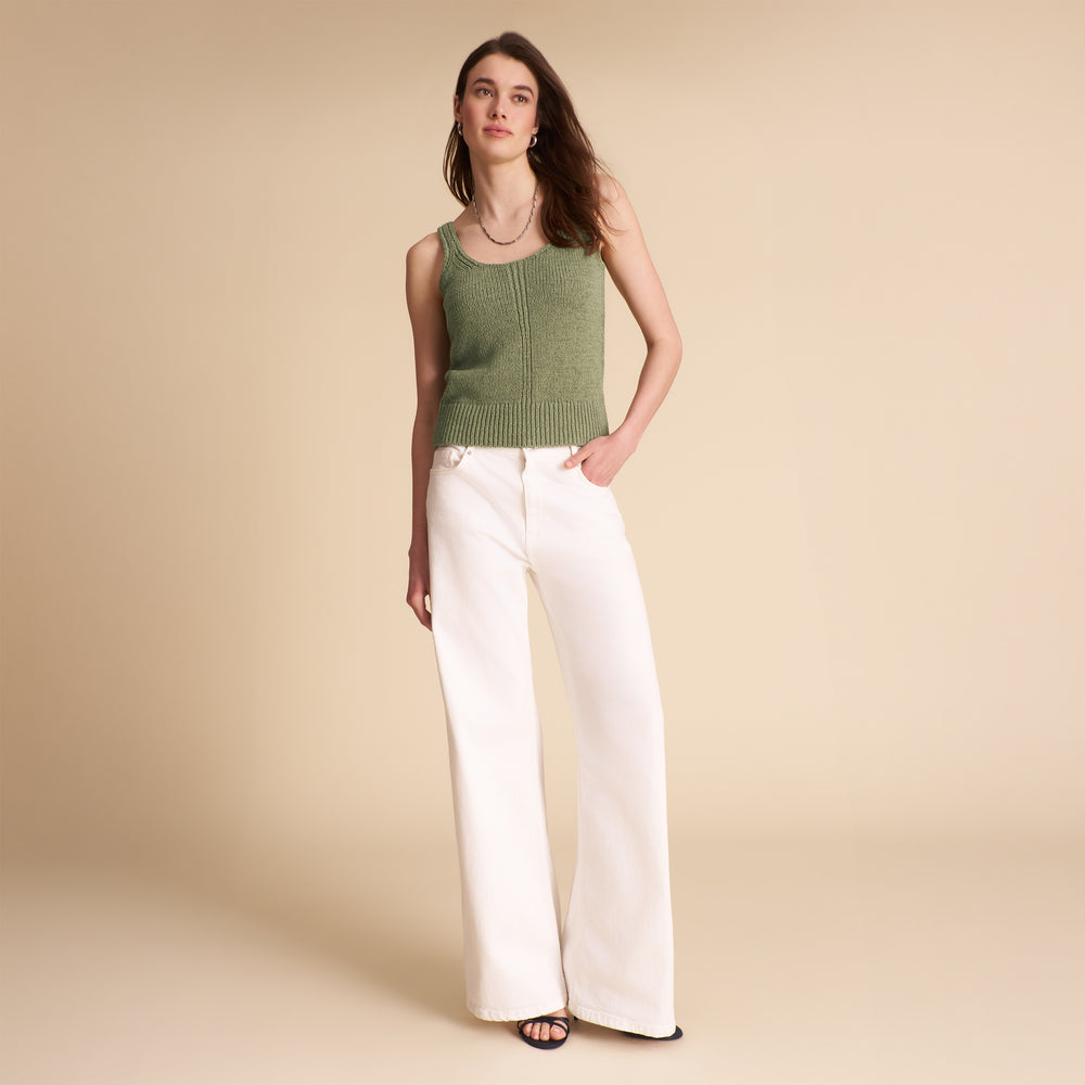 Woman wearing a green sleeveless top and white pants on a beige background