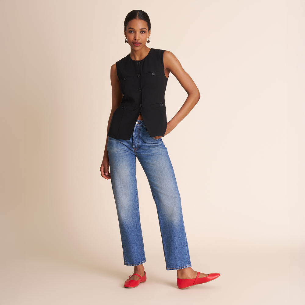 Woman wearing a black sleeveless top and blue jeans on a beige background
