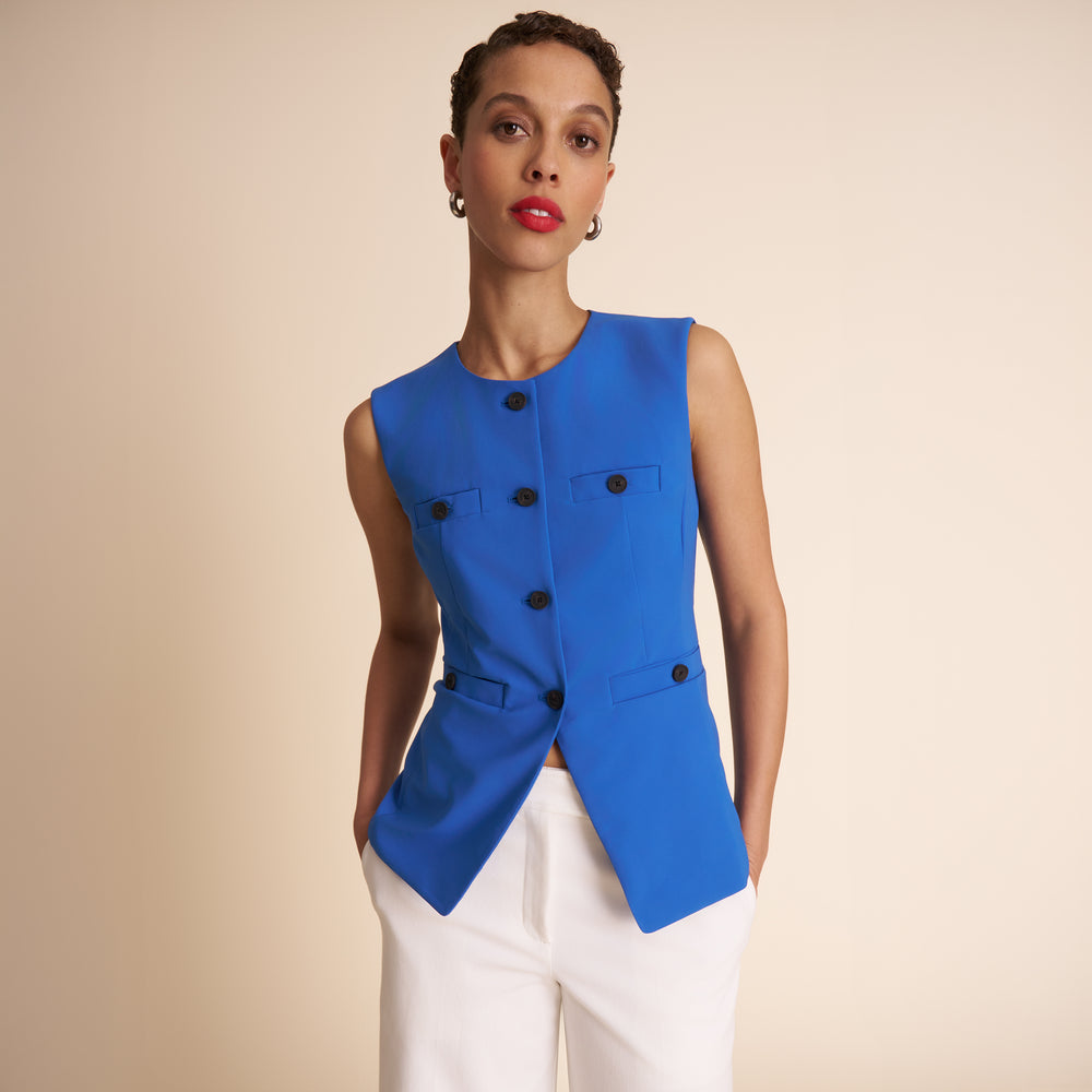 Woman wearing a blue vest with black buttons on a beige background