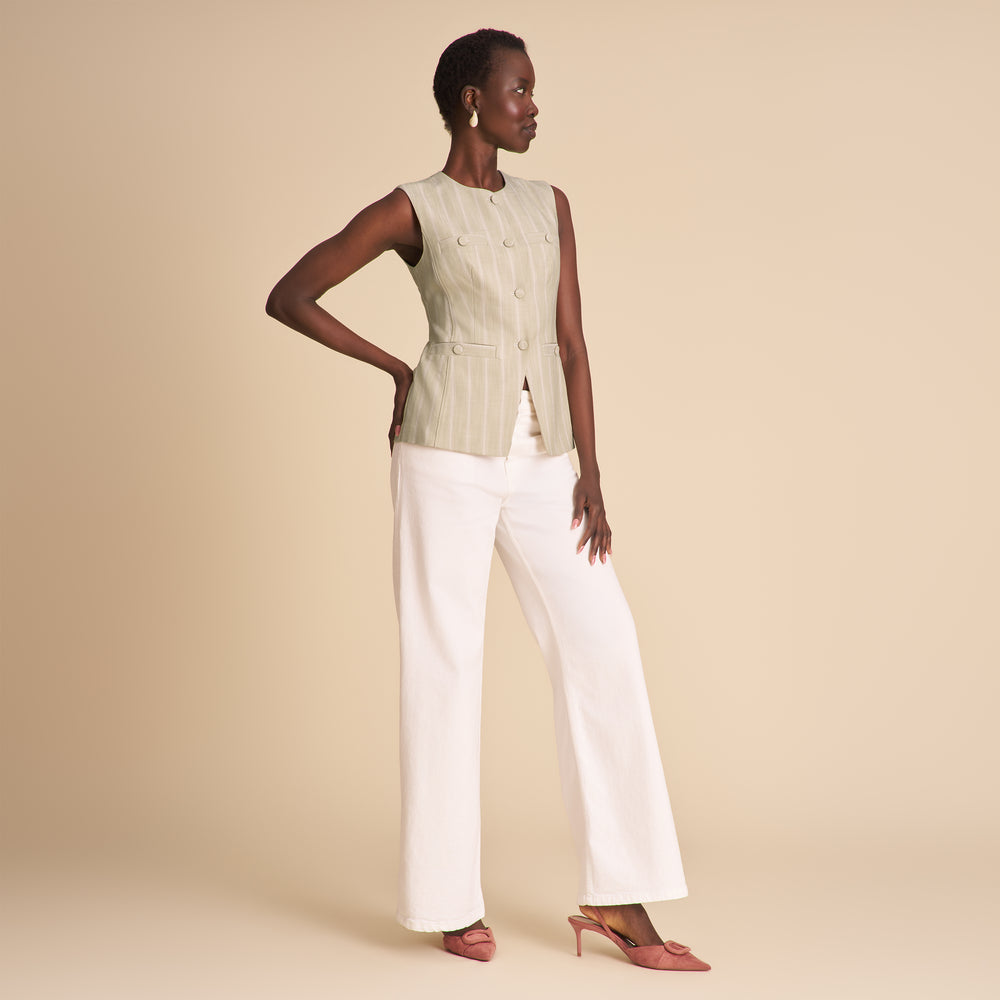 Woman wearing a light green sleeveless top and white pants on a beige background