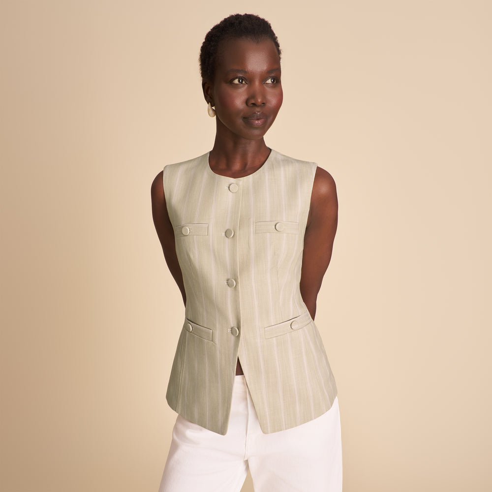 Woman wearing a beige vest over a white top on a beige background