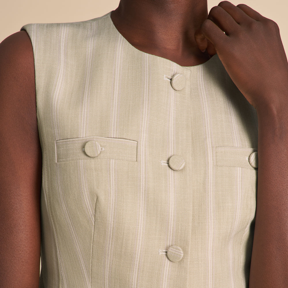 Close-up of a person wearing a light-colored vest with buttons and a pocket.
