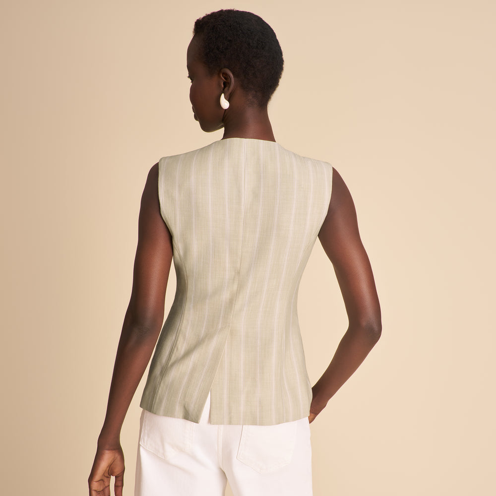 Woman wearing a sleeveless, light-colored top with vertical stripes on a beige background