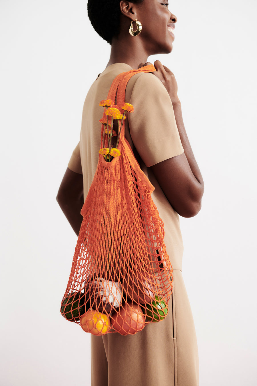 image of a woman wearing the annika top and elena culotte in light saddle holding a mesh bag of fruit