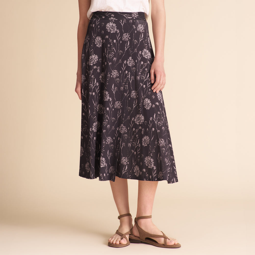 Woman wearing a dark floral skirt and white tee on a beige background