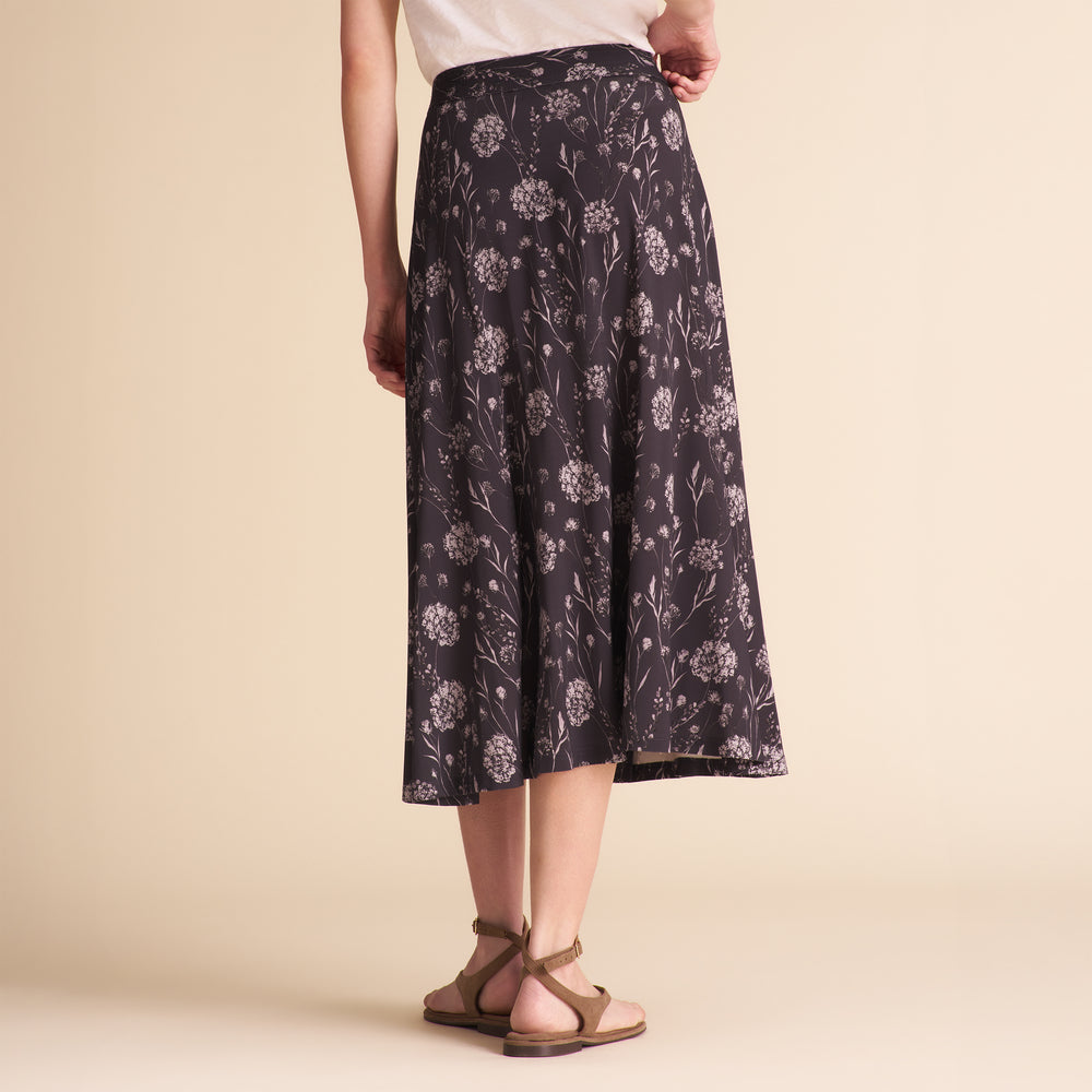 Woman wearing a dark floral skirt and white tee on a beige background