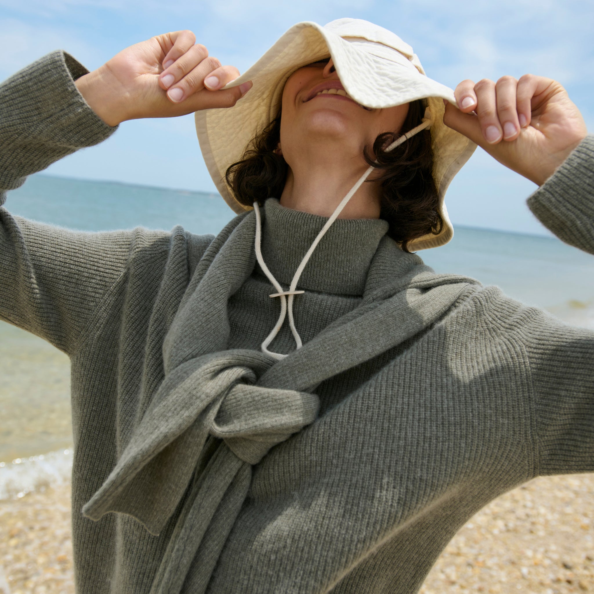 mood image of a woman on a beach wearing the arbus sweater in dark moss