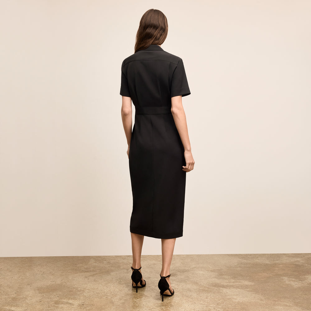 Woman wearing a black dress standing against a beige background