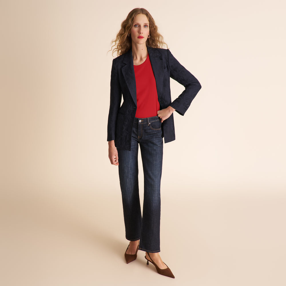 Woman wearing a navy blazer, red shirt, and jeans on a beige background