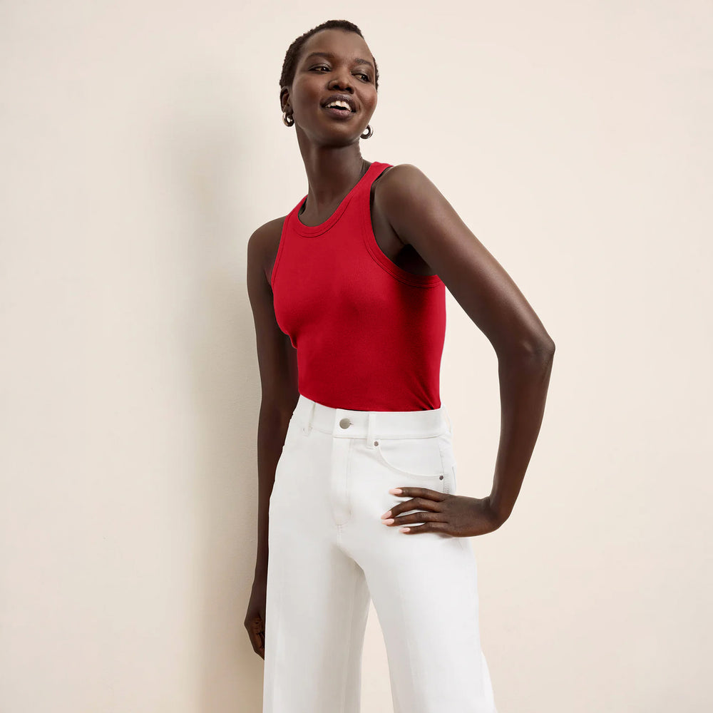 Woman wearing a red tank top and white pants against a beige background