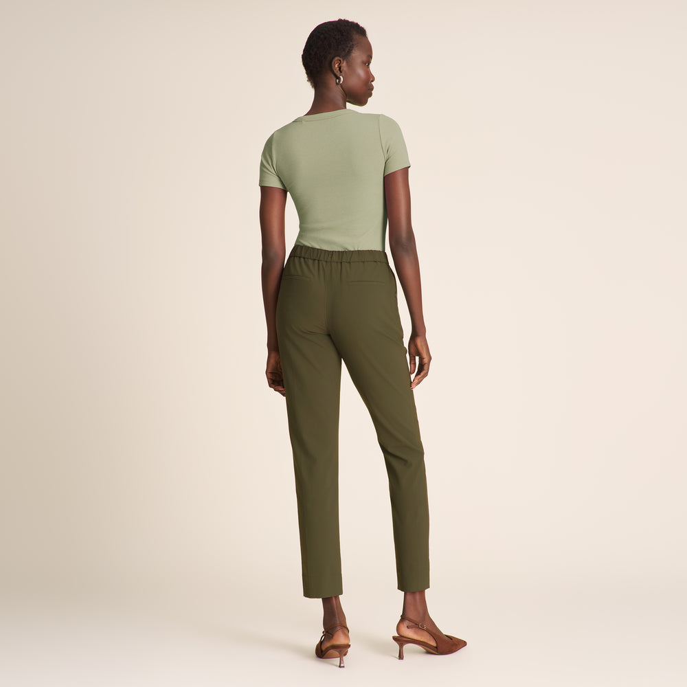 Woman wearing a green top and olive green pants on a beige background