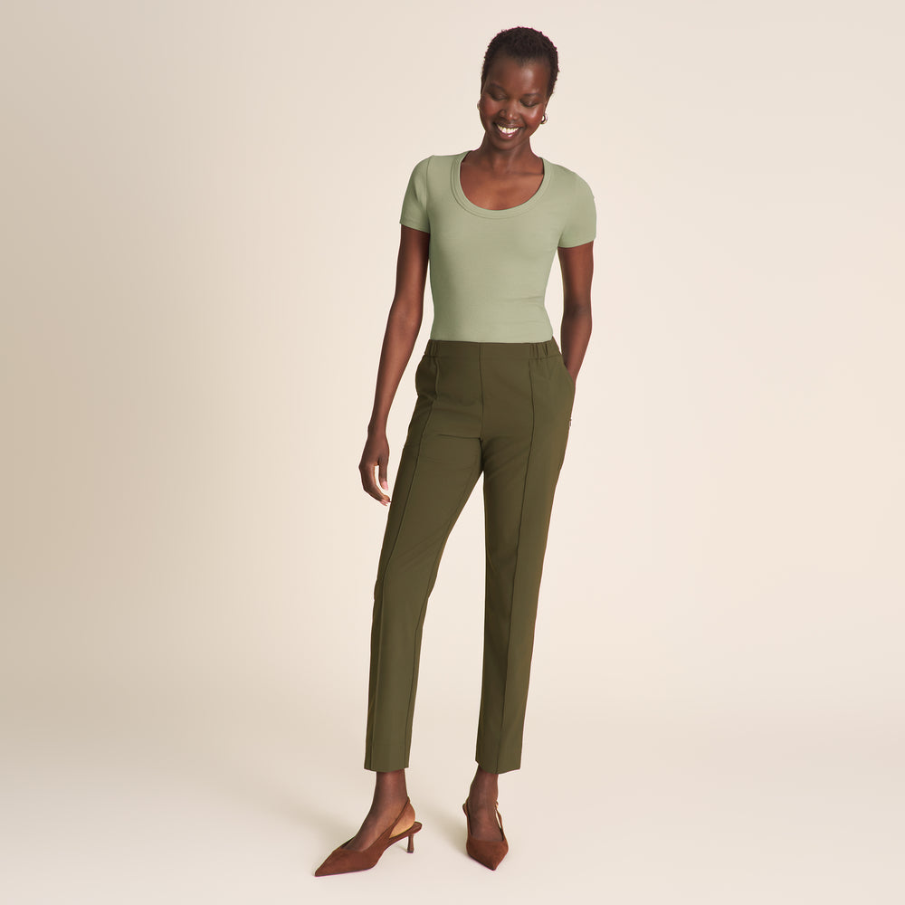 Woman wearing a green top and olive green pants on a beige background