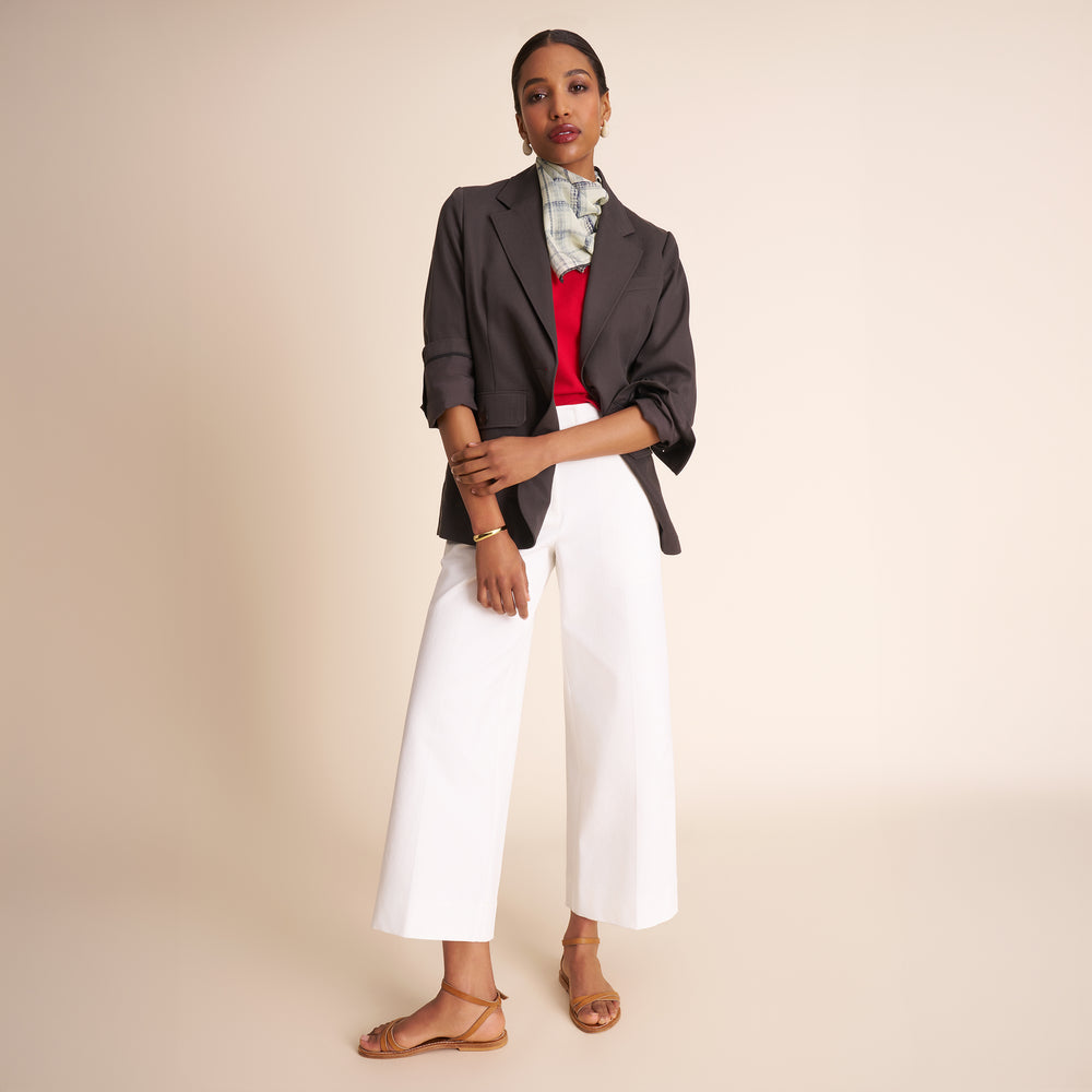 Woman wearing a gray blazer, red top, and white pants on a beige background