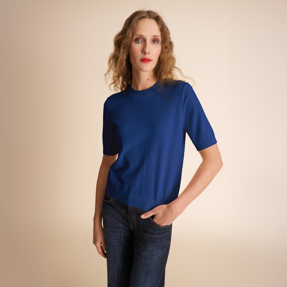 Woman wearing a blue t-shirt and jeans against a beige background