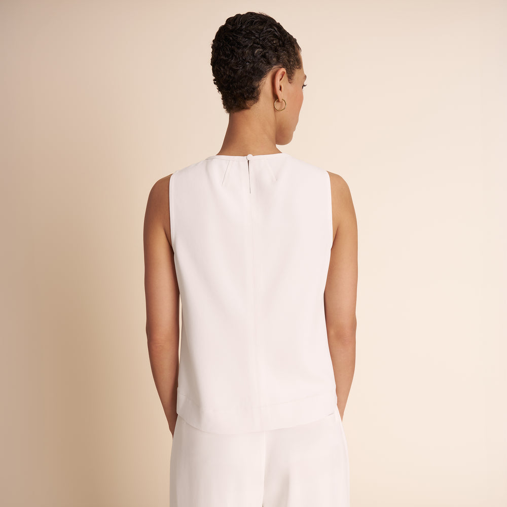 Woman wearing a white sleeveless dress against a beige background