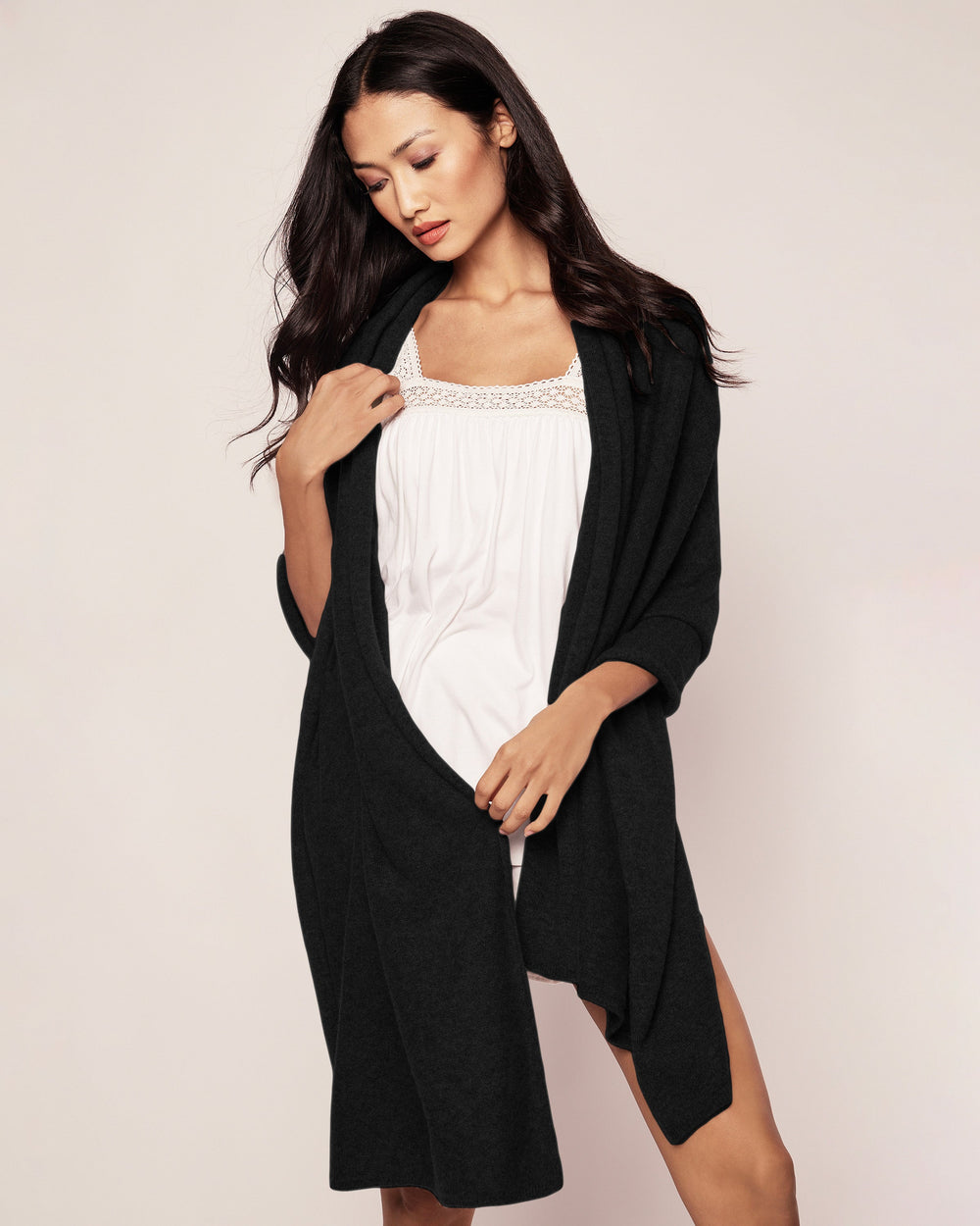 Woman wearing a black cardigan over a white top on a plain background