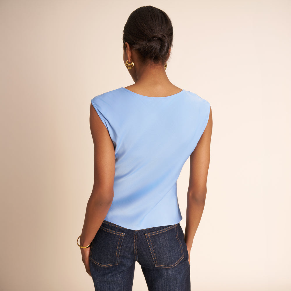 Person wearing a light blue sleeveless top and dark blue jeans on a beige background