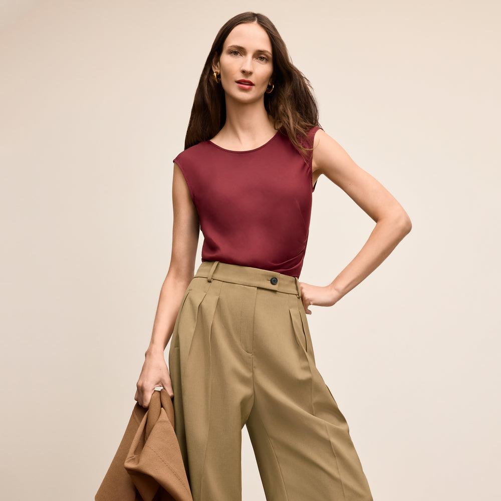 Woman wearing a burgundy top and beige pants against a beige background