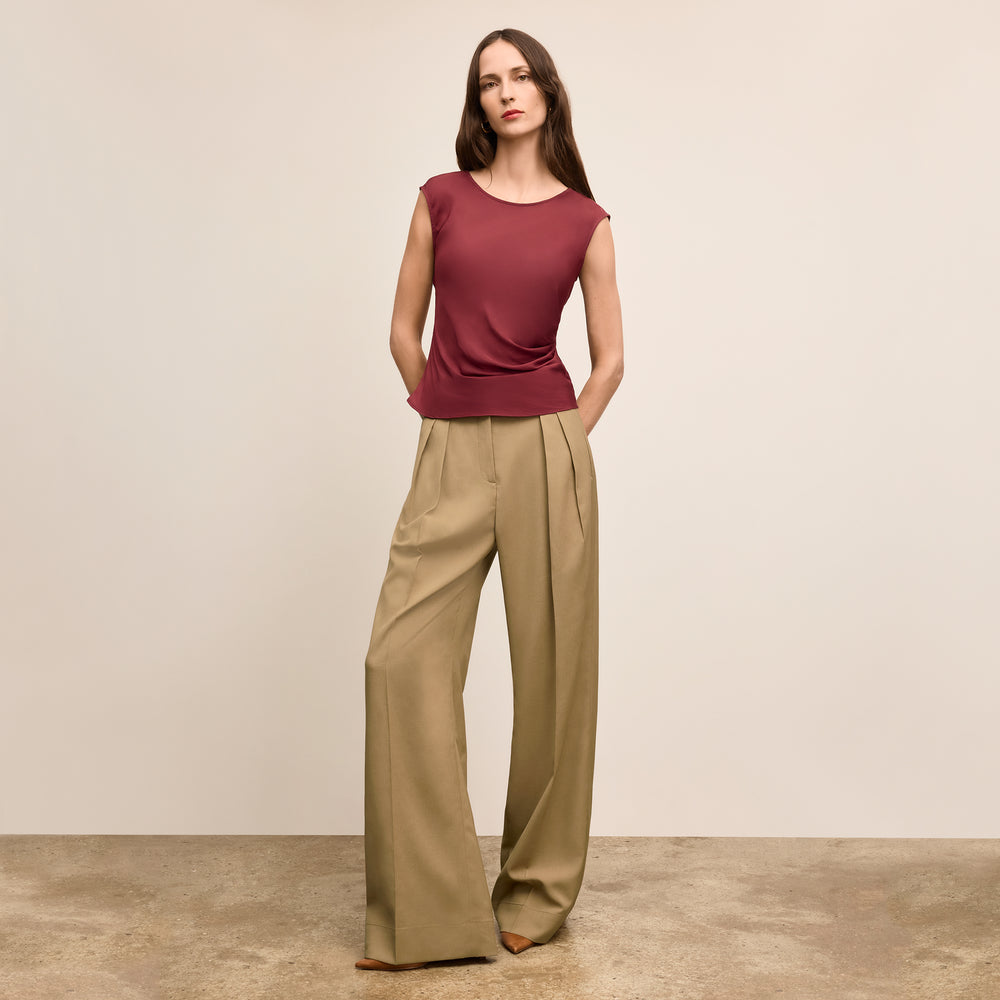 Woman wearing a maroon sleeveless top and beige wide-leg pants against a plain background