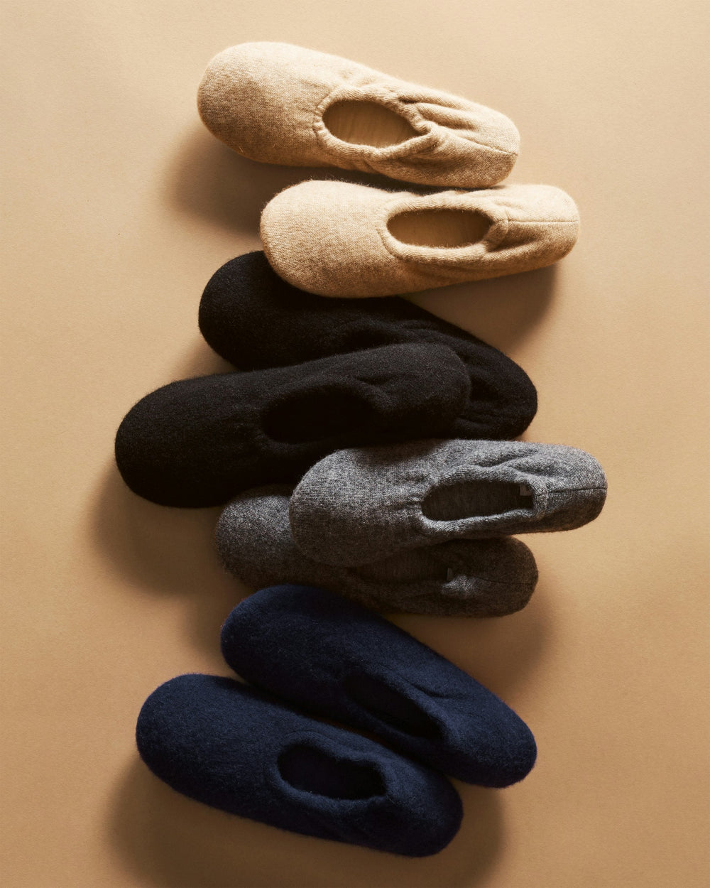 Set of four pairs of slippers in beige, black, gray, and navy on a beige background