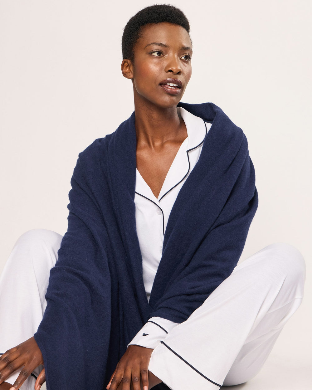 Person wearing a navy blue robe over a white shirt and pants on a light background