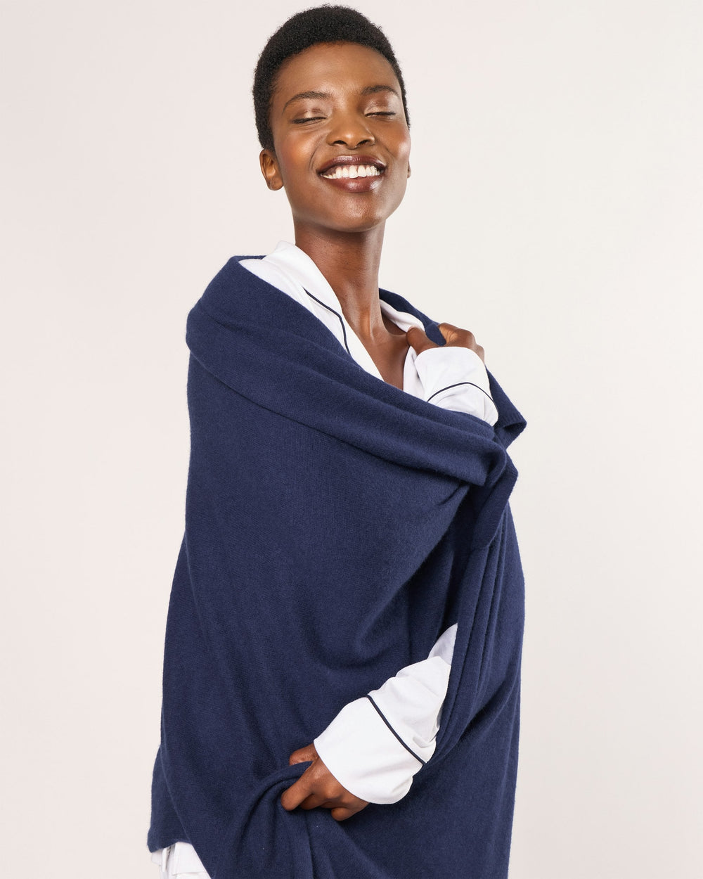 Person wearing a navy blue shawl over a white shirt on a beige background