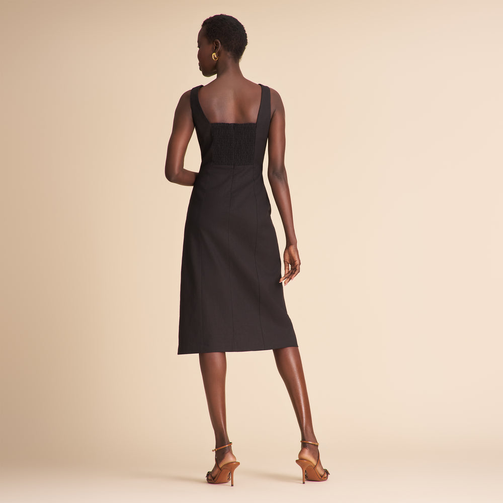 Woman wearing a black linen dress with black buttons on a beige background
