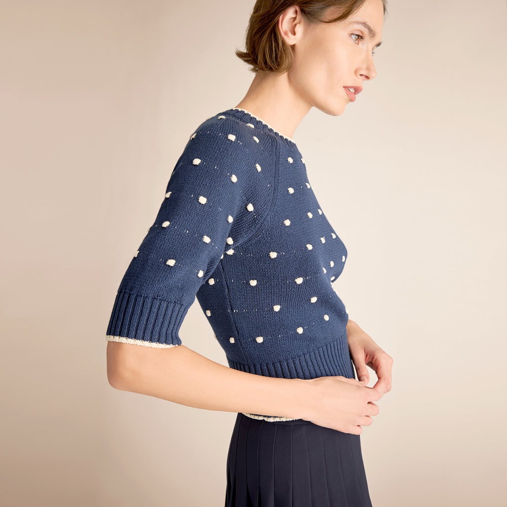 Woman wearing a blue polka dot sweater against a beige background